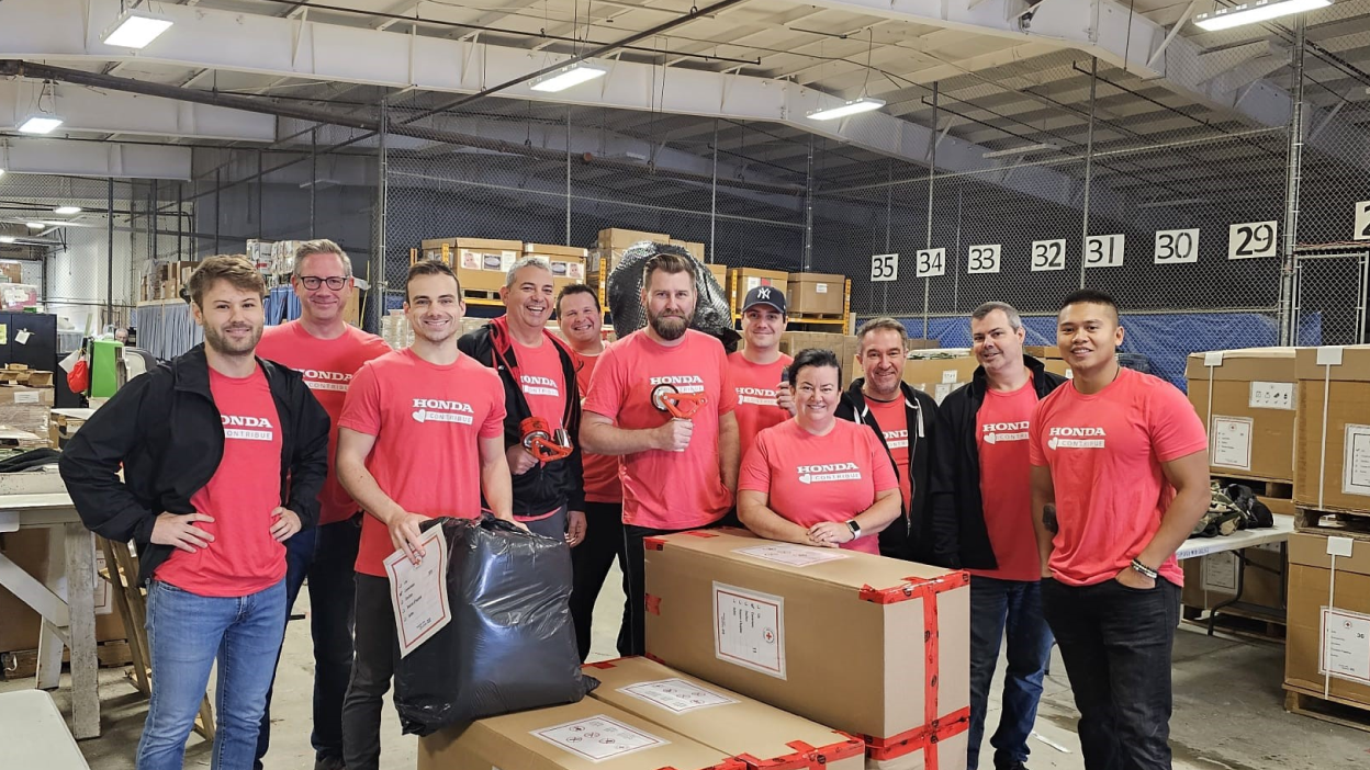 A group of employees in Team Honda t-shirts pose in a warehouse. 
