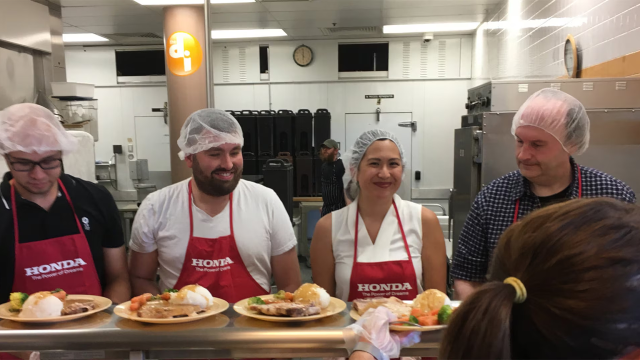 Honda employees are shown in red aprons working in a meal kitchen. 