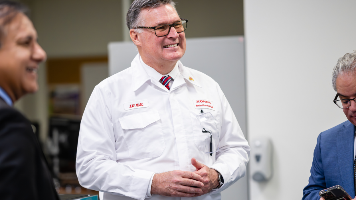 A male Honda staff member in a lab coat is smiling and interacting with two other people.