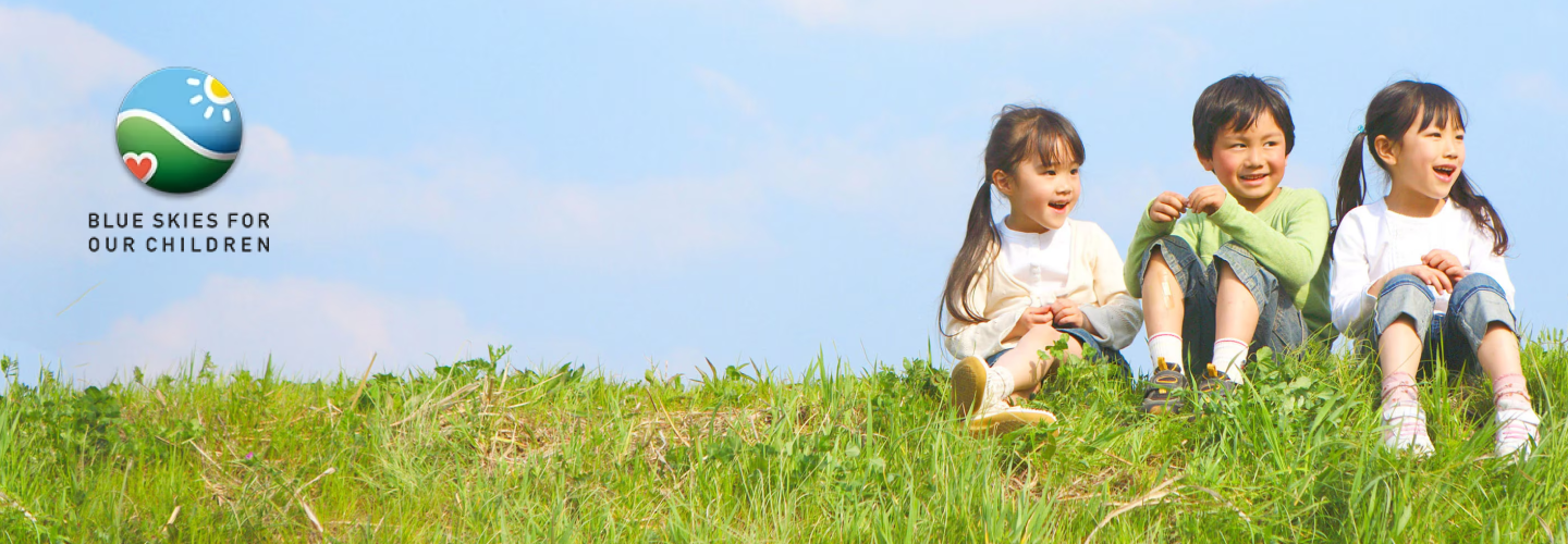 Three young children sit smiling on a grassy hill in the sunshine, 