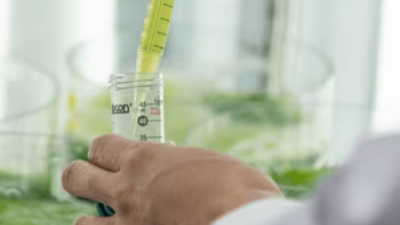 Close-up of a hands as they use a dropper to add liquid to a beaker.