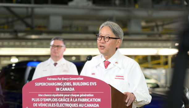 A Honda spokesperson in a white coat makes an announcement from a podium. 