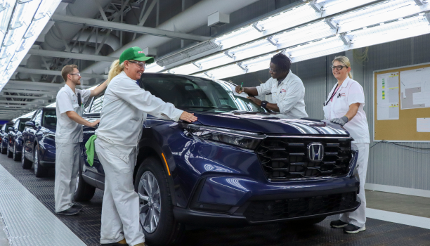 A group of Honda workers stand on the line wearing white coats and smiling.