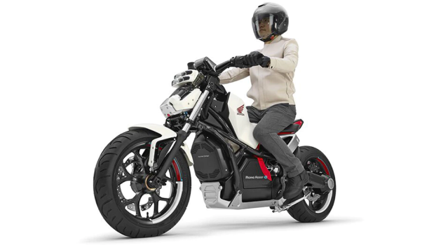 A person straddles a Honda Riding Assist-e motorcycle in a white space. 